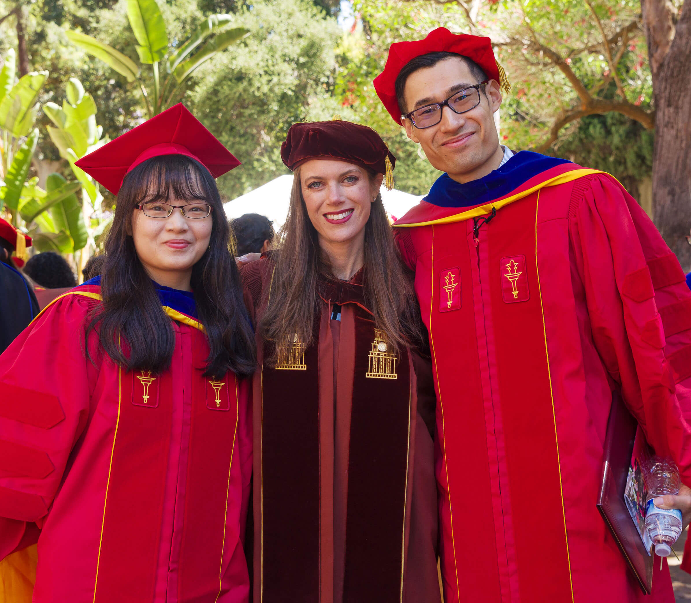 凯利·桑德斯教授(Kelly Sanders)在南加州大学联合公园(USC’s Associates Park)举行的就职典礼和颁奖招待会上，身旁站着刚戴上兜帽的博士李云(Yun Li)和陈默(Mo Chen)。